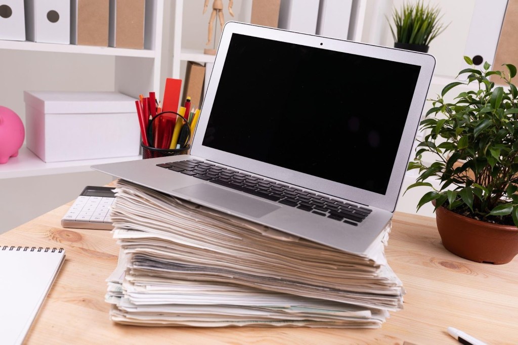 Cadastro escolar: como economizar recursos e ser mais eficiente? 2 Foto de pilha de papeis e computador