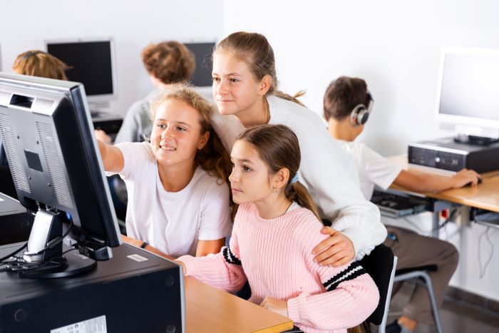Foto de estudantes olhando para tela de computador em laboratório de informática, representando a inclusão digital nas escolas.