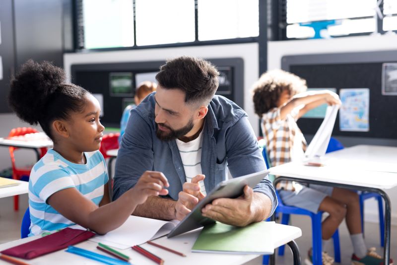 Veja 7 propostas para melhorar sua escola 1 Foto de professor solucionando dúvida de aluna na sala de aula, com a ajuda de um tablet.