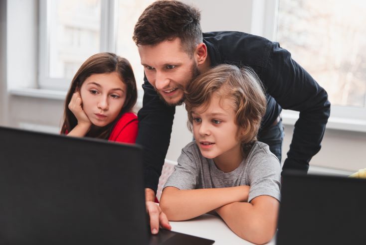 Qual é o papel do professor na era da Educação 5.0? 1 Foto de professor orientando dois estudantes em atividade online no notebook.