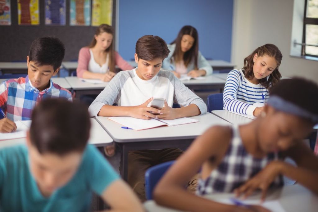 Foto de estudante utilizando celular em sala de aula.
