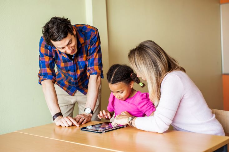 Tarefa de casa: como torná-la mais significativa? 4 Foto de menina fazendo tarefa de casa em plataforma digital, acompanhada pelos pais