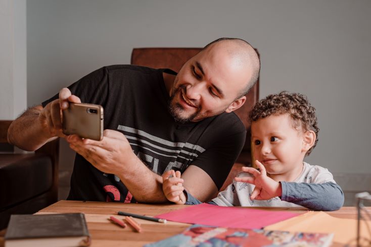 Como aproximar a família da escola e fortalecer a relação de parceria? 3 Foto de pai e filho vendo tarefa de casa em aplicativo de comunicação escolar