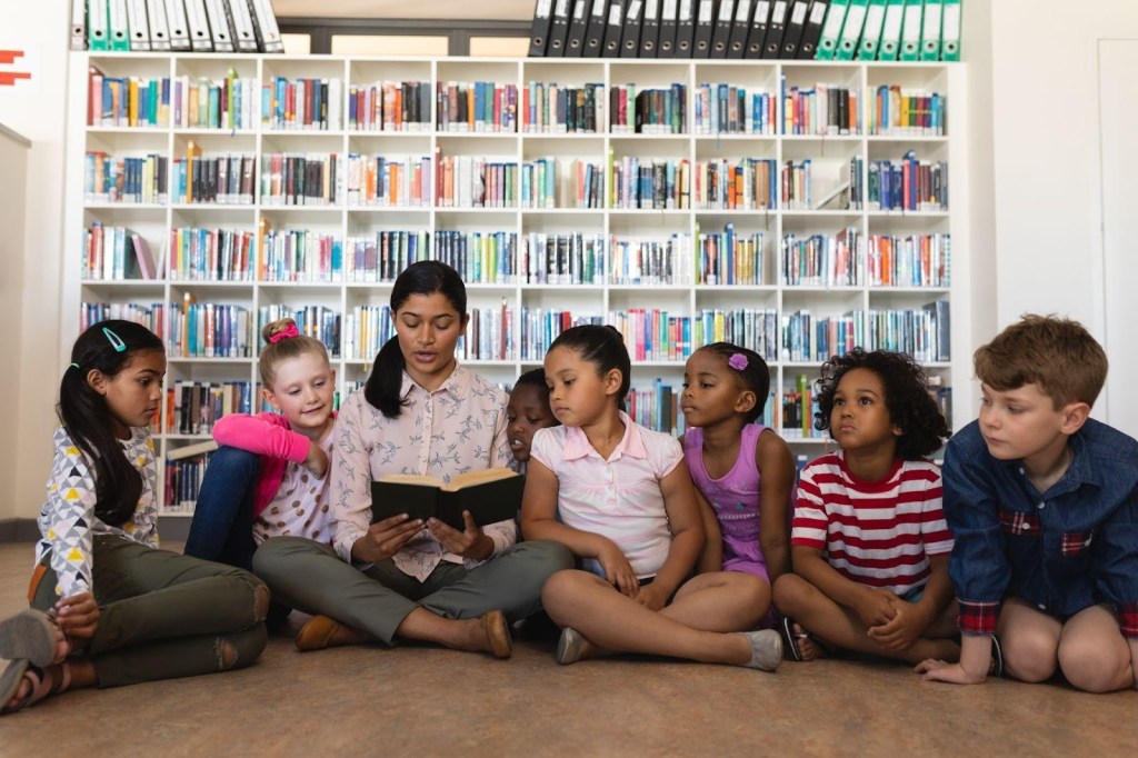Leitura Infantil: quando começar e quais gêneros escolher? 1 Foto de professora lendo para crianças na biblioteca